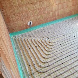 Elektro System - Rozłożona instalacja ogrzewania podłogowego na warstwie izolacyjnej, widoczne rury grzewcze mocowane spinkami, ściany z cegły ceramicznej.