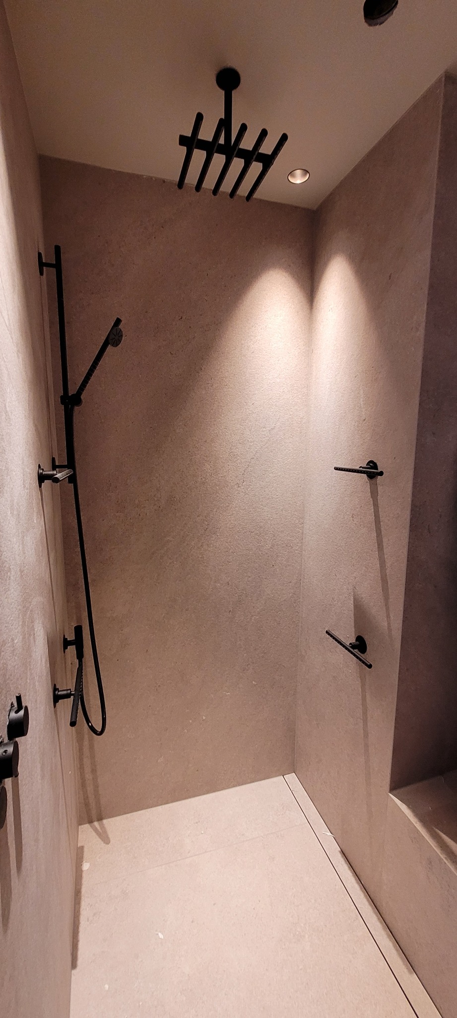 Nowoczesna kabina prysznicowa z deszczownicą w kolorze czarnym, minimalistyczne półki na ręczniki i armatura w odcieniach beżu.