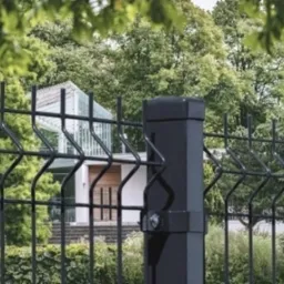 Czarne, panelowe ogrodzenie na tle zieleni i nowoczesnego domu z białymi elementami, widok z bliska, spokojna kolorystyka.