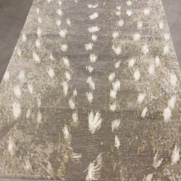 Sonia Świerlikowska - Dywan w odcieniach szarości i beżu z abstrakcyjnym wzorem przypominającym ślady zwierząt, leżący na szarej, betonowej podłodze.