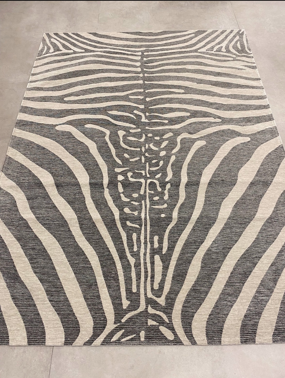 Nowoczesny dywan o wzorze inspirowanym skórą zebry, z centralnym motywem przypominającym kręgosłup, leżący na jasnej, gładkiej podłodze.