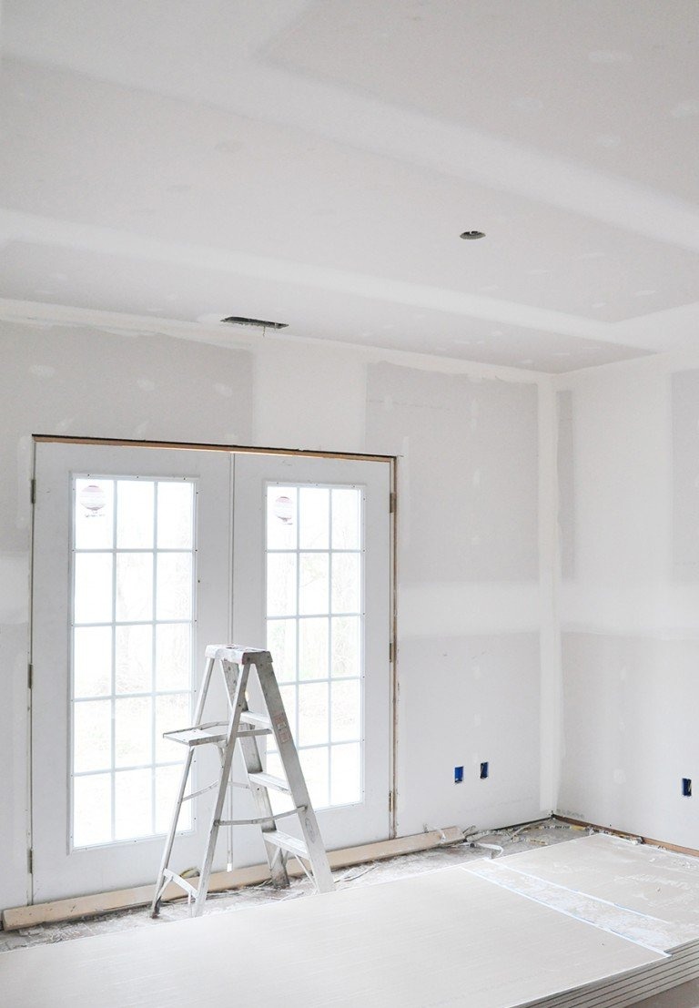 Wnętrze w trakcie remontu: ściany pokryte gładzią szpachlową, białe dwuskrzydłowe drzwi balkonowe z szybami, aluminiowa drabina przystawna, widoczne puszki elektryczne w ścianie.