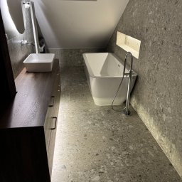 Kamil Malinowski - Nowoczesna łazienka na poddaszu z wanną, umywalką na szafce z ciemnego drewna i szarą mozaikową okładziną ścian i podłogi. Oświetlenie LED podkreśla detale.