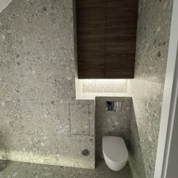 Kamil Malinowski - Wykończona łazienka z szarą mozaiką na ścianach i podłodze, podwieszana toaleta, szafka nad toaletą z oświetleniem LED. Nowoczesny design.