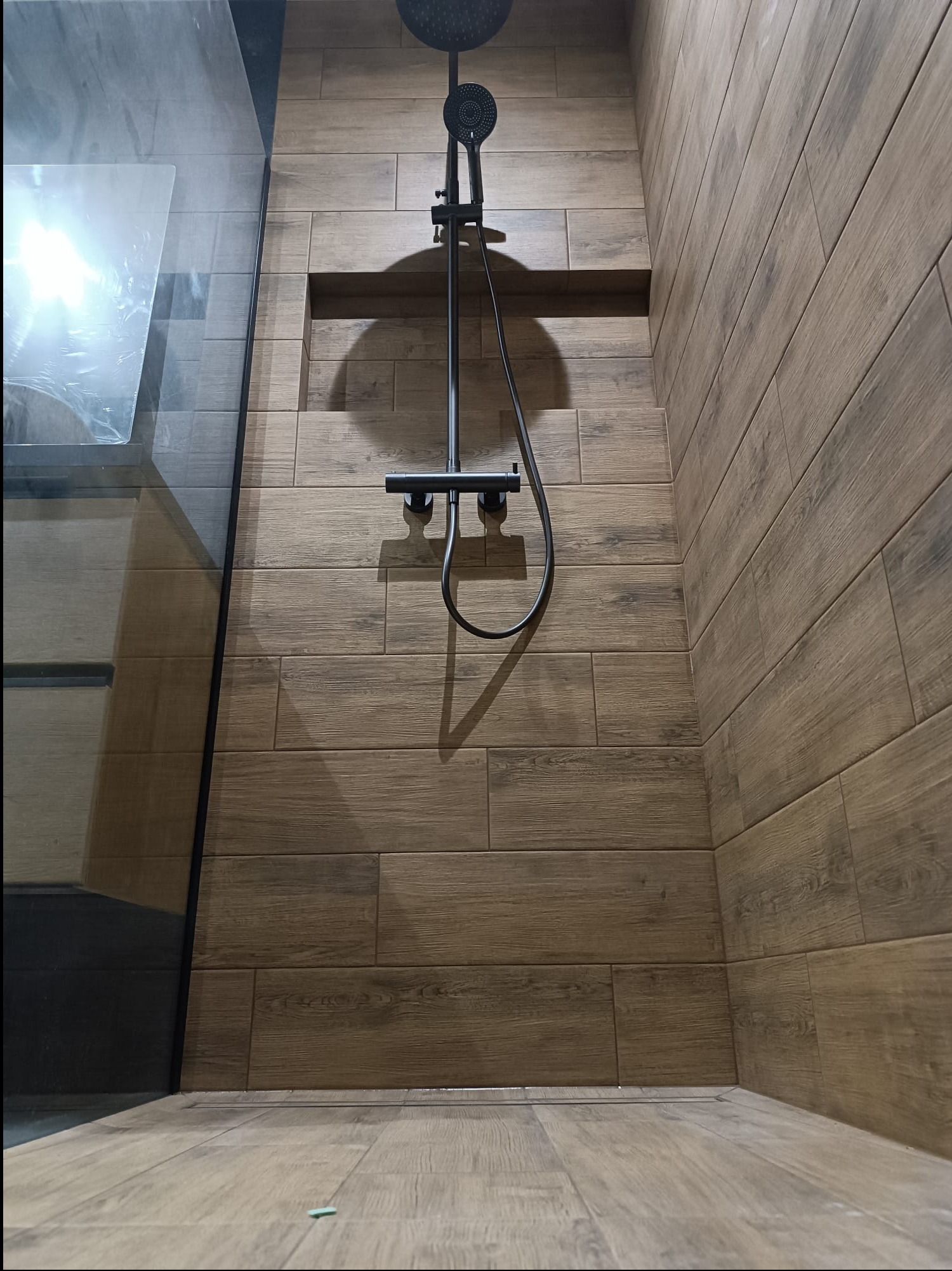 Nowoczesny prysznic z deszczownicą w wykończeniu imitującym drewno, z wnęką w ścianie i szklaną kabiną.