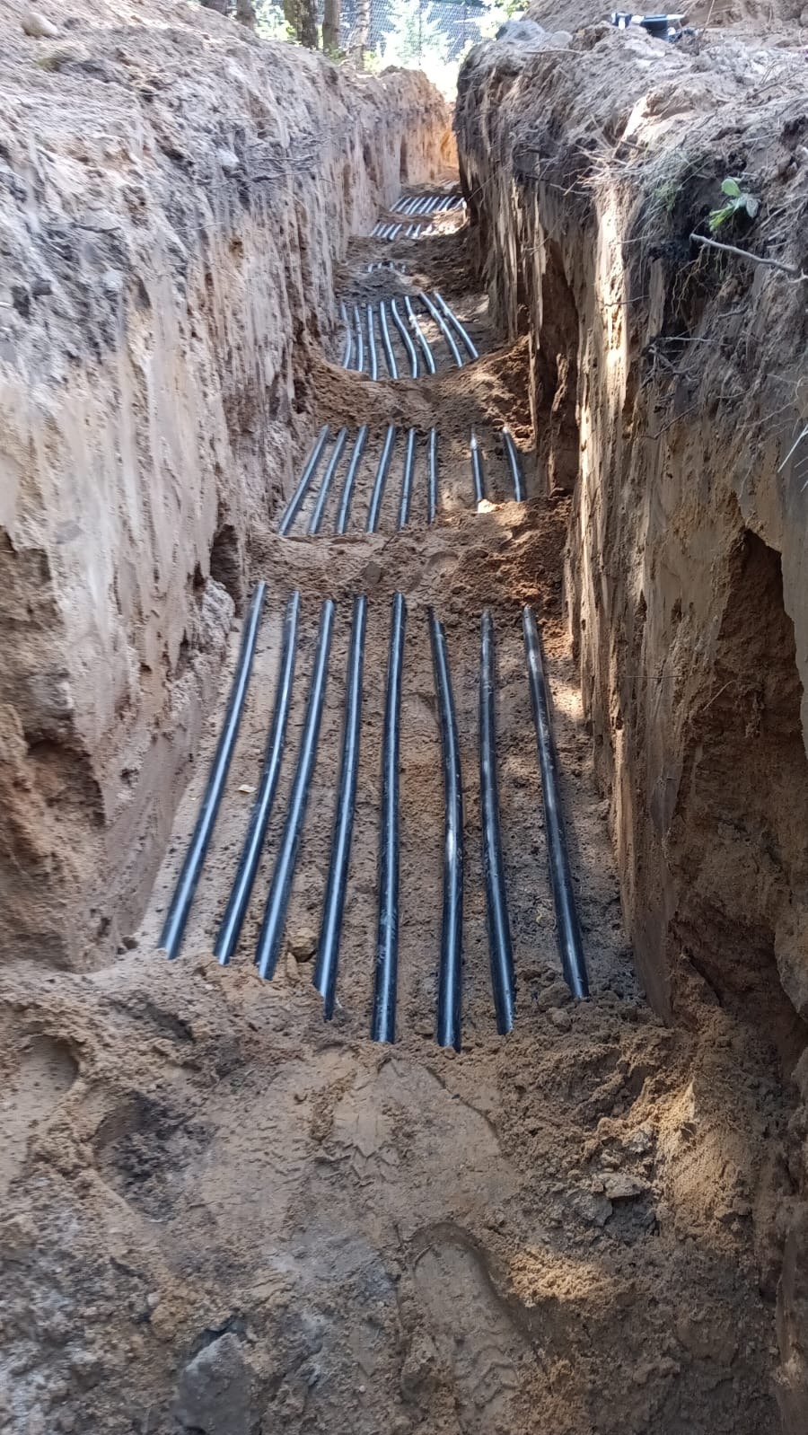 Rury w wykopie, instalacja poziomego kolektora gruntowego pompy ciepła. Równoległe rury ułożone w ziemi, widok z góry na wykop.