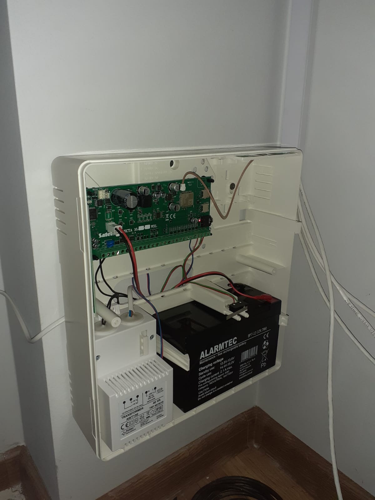 Otwarta obudowa centrali alarmowej z widoczną płytą główną Satel ECTA 16 WRL, transformatorem AWT150 i akumulatorem Alarmtec BP7-12, zamontowana na ścianie.