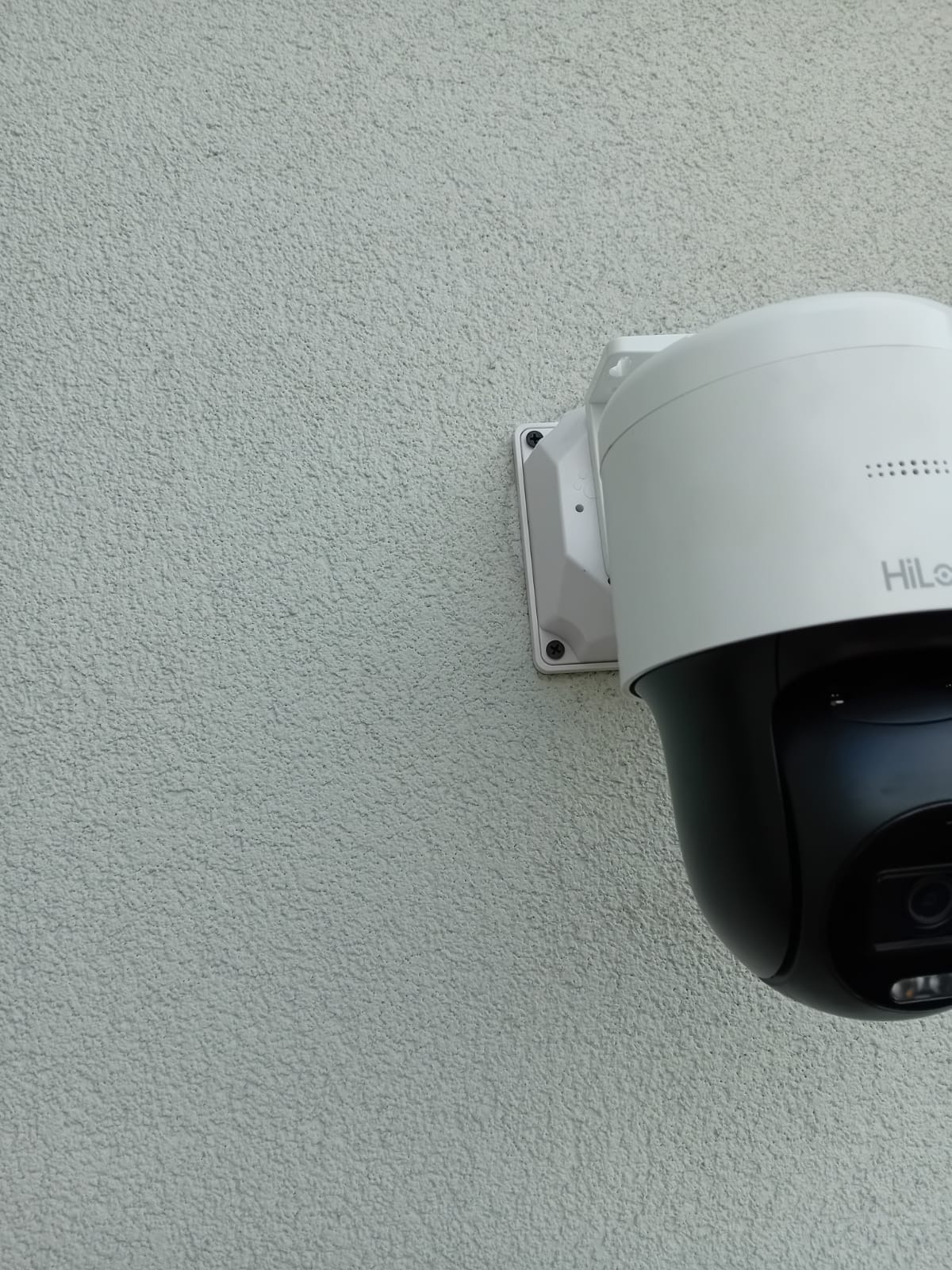 Zewnętrzna kamera PTZ Hikvision HiLook, zamontowana na teksturowanej, jasnej ścianie, widoczna z boku.