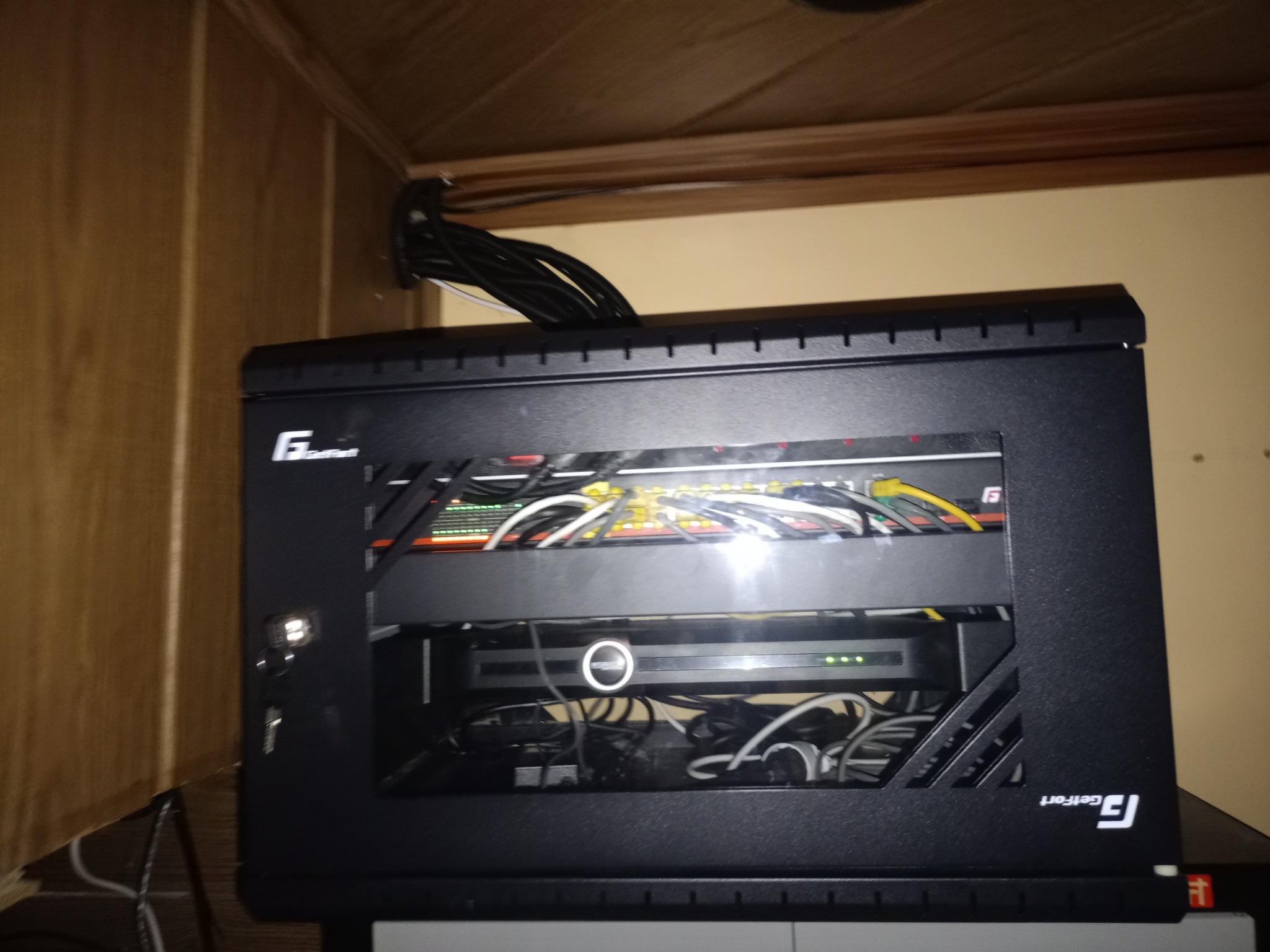 Czarna szafka rack zamontowana w szafce, widoczne kable i urządzenia sieciowe, oświetlenie LED wewnątrz, logo Geffort na obudowie.