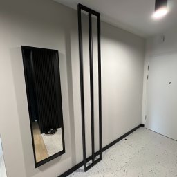 PERFECTBUD GROUP SPÓŁKA Z OGRANICZONĄ ODPOWIEDZIALNOŚCIĄ - Nowoczesny przedpokój z lustrem w czarnej ramie i dekoracyjną ścianką z czarnych listew. Białe ściany i podłoga w stylu lastryko. Minimalistyczny design.