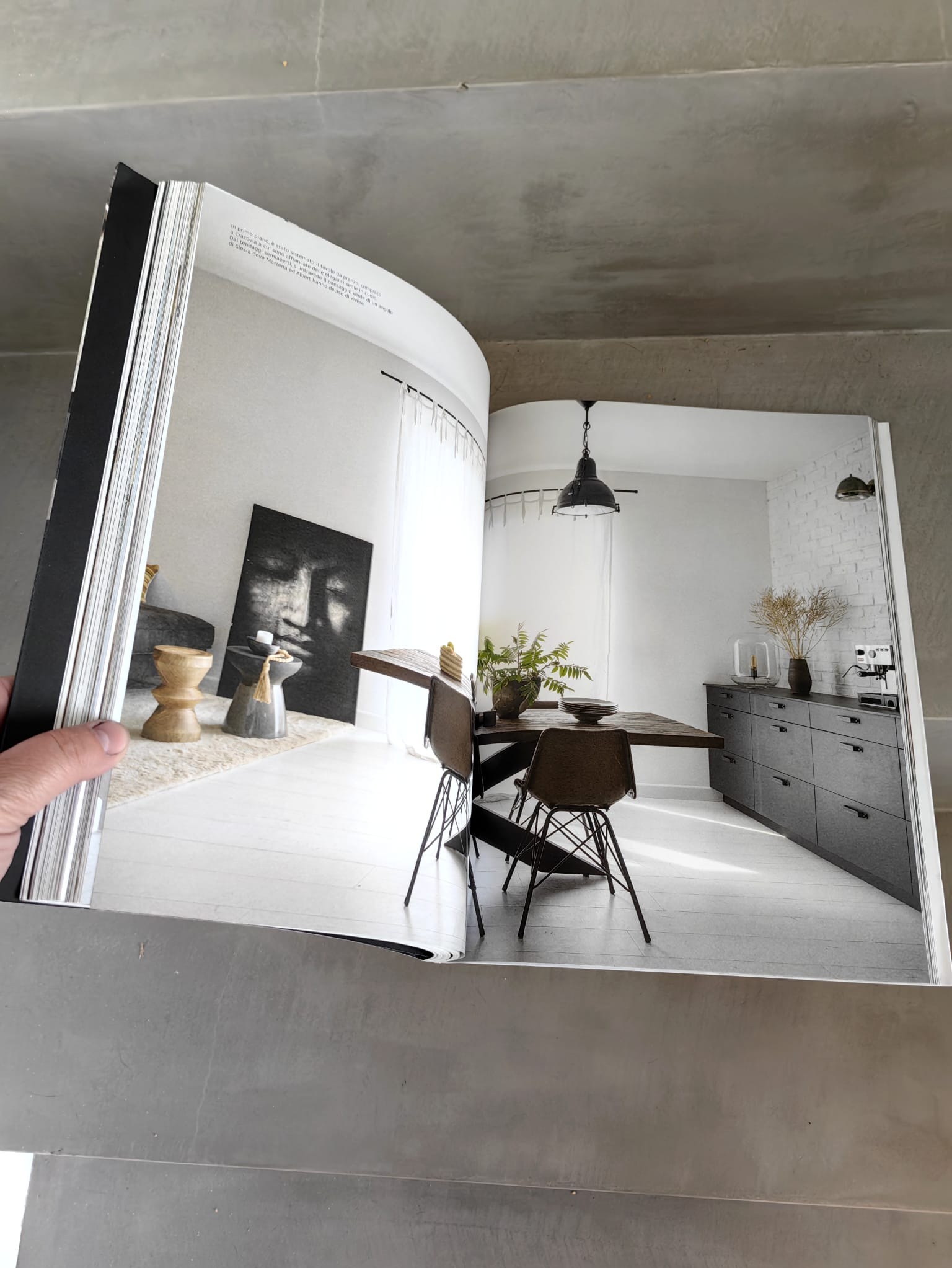 Otwarta książka prezentuje wnętrze w stylu skandynawskim: białe ściany, drewniany stół z krzesłami, szara komoda i minimalistyczne dekoracje. Widoczny fragment tekstu.