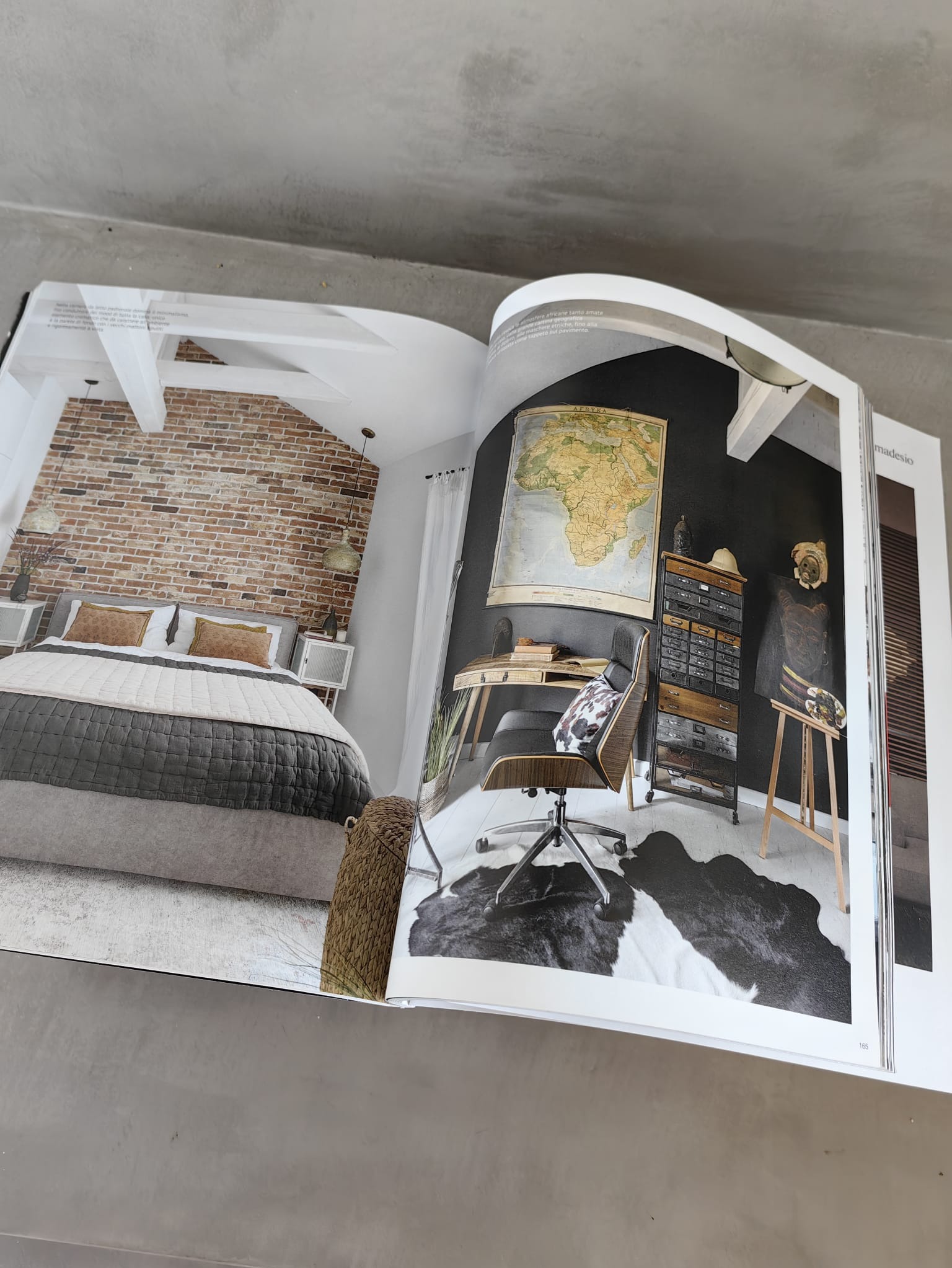 Otwarta książka prezentuje aranżację wnętrza: sypialnia z ceglaną ścianą i biuro z mapą Afryki. Widoczne meble, dekoracje i oświetlenie. Styl eklektyczny.
