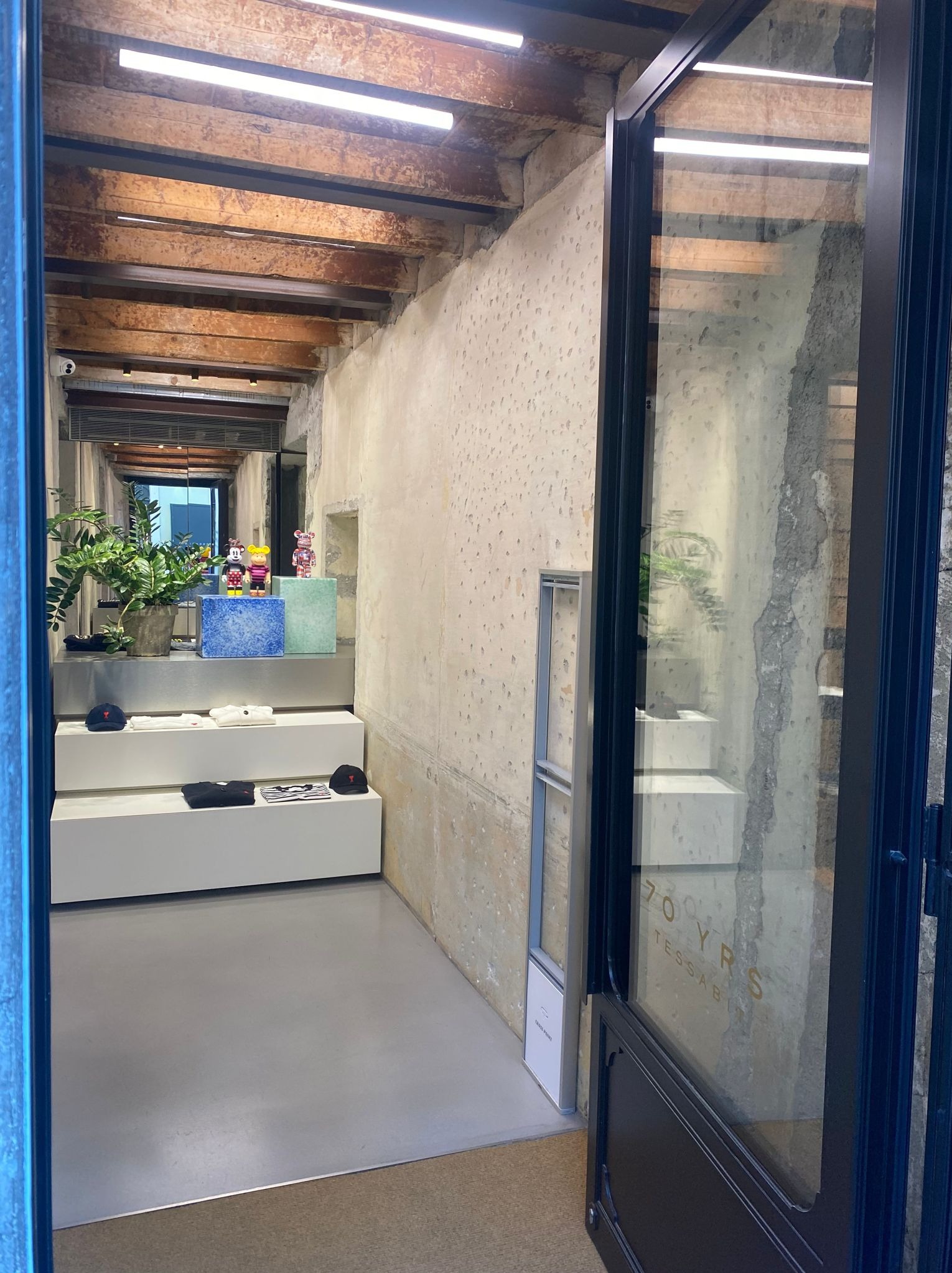 Wnętrze sklepu w Warszawie z surowymi ścianami, drewnianym stropem z widocznymi belkami i nowoczesnym oświetleniem, prezentujące minimalistyczny design z ekspozycją ubrań i dekoracji.