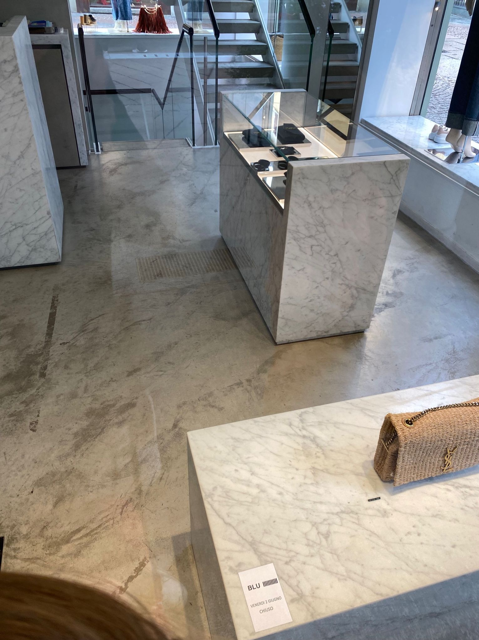 Wnętrze sklepu z marmurowymi elementami: podłoga, schody, ekspozytory i stoliki, na jednym z nich leży torebka. Widoczne detale wykończenia.