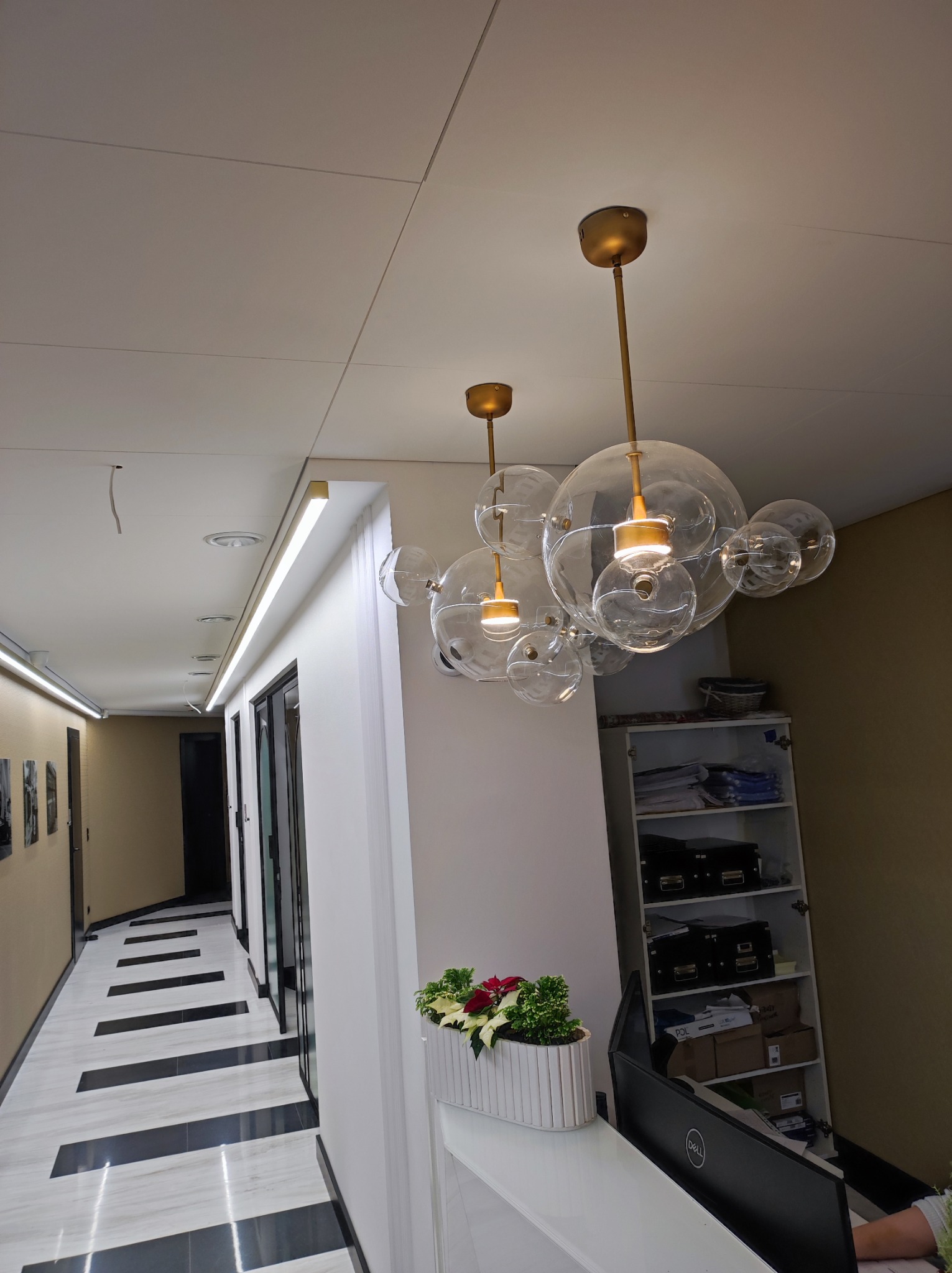 Nowoczesny hol z designerską lampą sufitową w kształcie bąbelków, białymi ścianami, podłogą w czarno-białe pasy i dekoracyjnym oświetleniem LED.