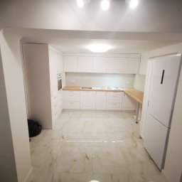 MK FURNITURE Michał Kalinowski - Wnętrze nowoczesnej, jasnej kuchni z białymi szafkami i drewnianymi blatami w Łomży, widok z perspektywy wejścia do pomieszczenia.