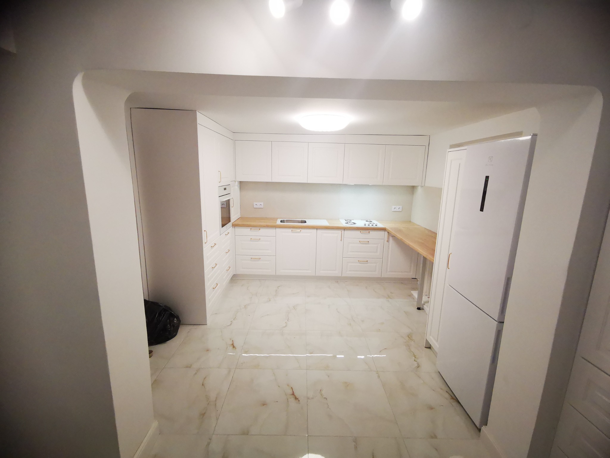 Wnętrze nowoczesnej, jasnej kuchni z białymi szafkami i drewnianymi blatami w Łomży, widok z perspektywy wejścia do pomieszczenia.