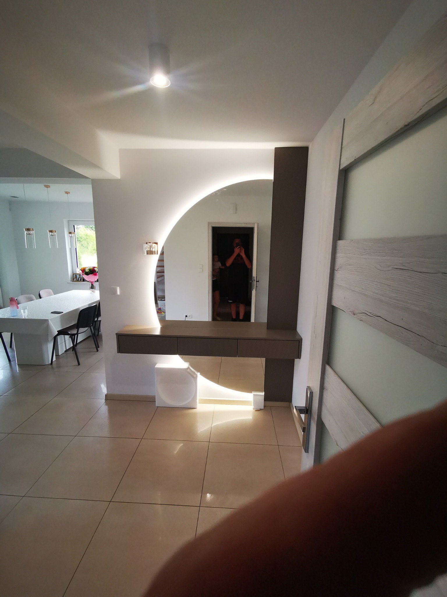 Nowoczesna toaletka z podświetlanym, okrągłym lustrem i szufladami, zrealizowana w Łomży, widoczna na tle jadalni z długim stołem i krzesłami.