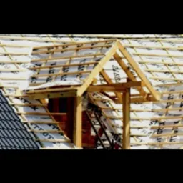 Widok na konstrukcję drewnianą dachu z widocznym oknem dachowym w trakcie budowy, z wykorzystaniem membrany dachowej i łat, częściowo pokryty dachówką.