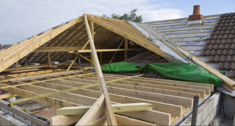 Konstrukcja drewniana nowego dachu w trakcie budowy, widoczne elementy więźby dachowej, fragment pokrycia dachowego z dachówki oraz komin w tle.