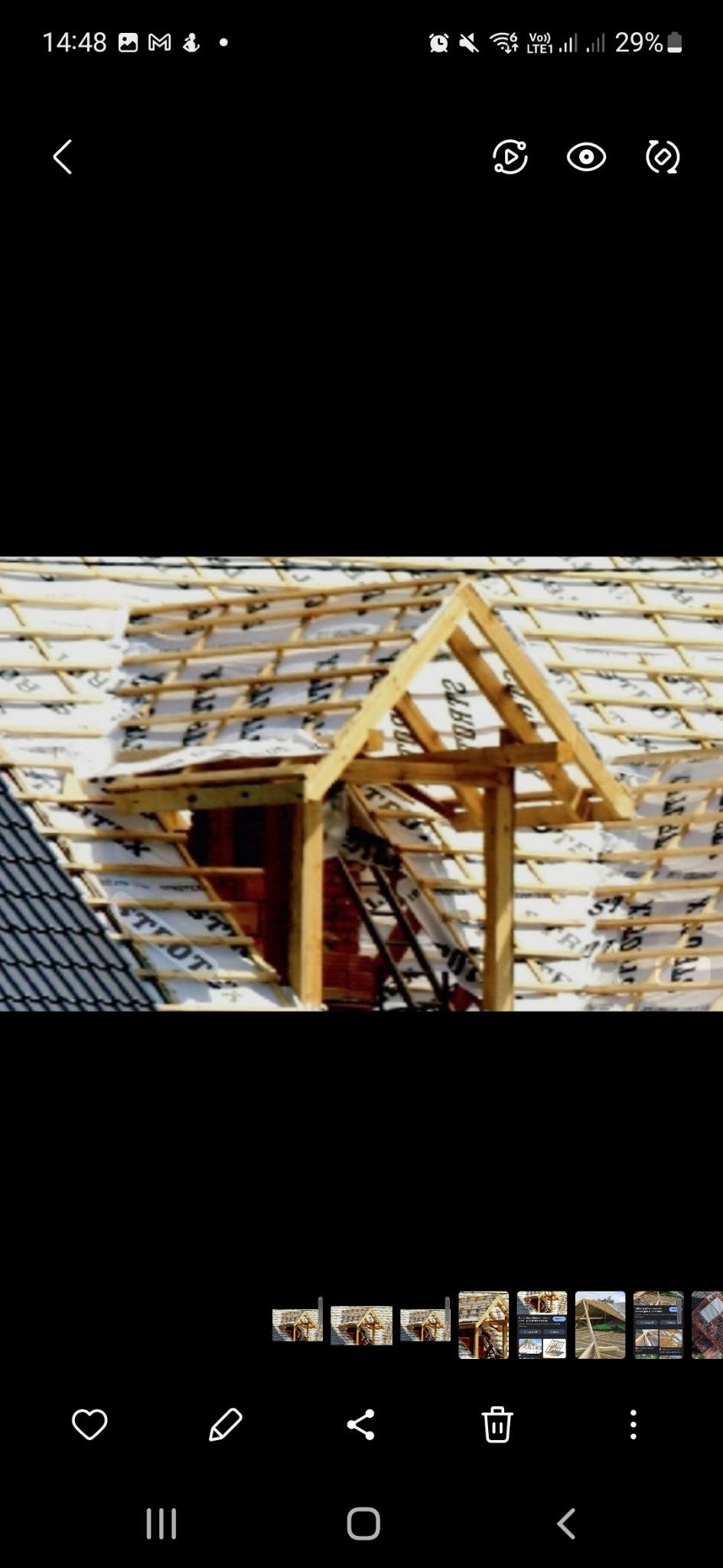 Widok na konstrukcję drewnianą dachu z widocznym oknem dachowym w trakcie budowy, z wykorzystaniem membrany dachowej i łat, częściowo pokryty dachówką.