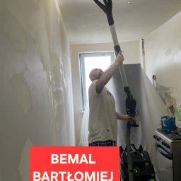 Bemal Bartłomiej Sikora - Pracownik szlifuje ścianę szlifierką teleskopową w trakcie prac wykończeniowych. Widoczny sprzęt i przygotowane ściany do malowania.