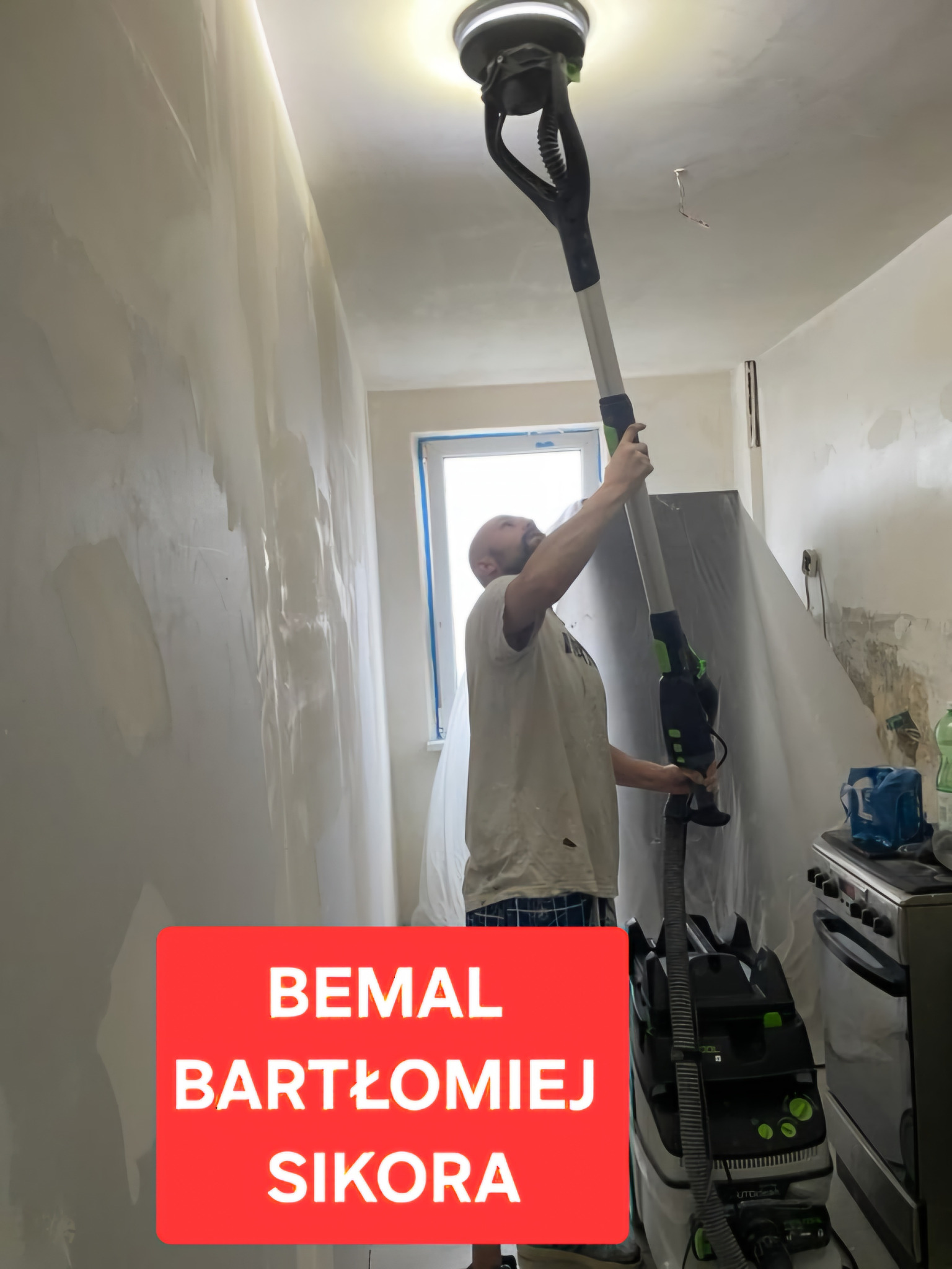 Pracownik szlifuje ścianę szlifierką teleskopową w trakcie prac wykończeniowych. Widoczny sprzęt i przygotowane ściany do malowania.