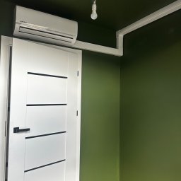 T- service Oleh Shablovskyi - Wnętrze z białą klimatyzacją Kaisai Eco nad drzwiami, biała instalacja elektryczna pod sufitem, zielone ściany i drewniana podłoga. Minimalistyczny design.