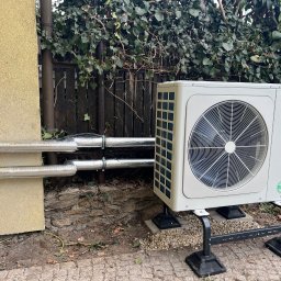 T- service Oleh Shablovskyi - Biała pompa ciepła York zamontowana na zewnątrz budynku z izolowanymi rurami, na tle ogrodzenia porośniętego bluszczem i kostki brukowej.