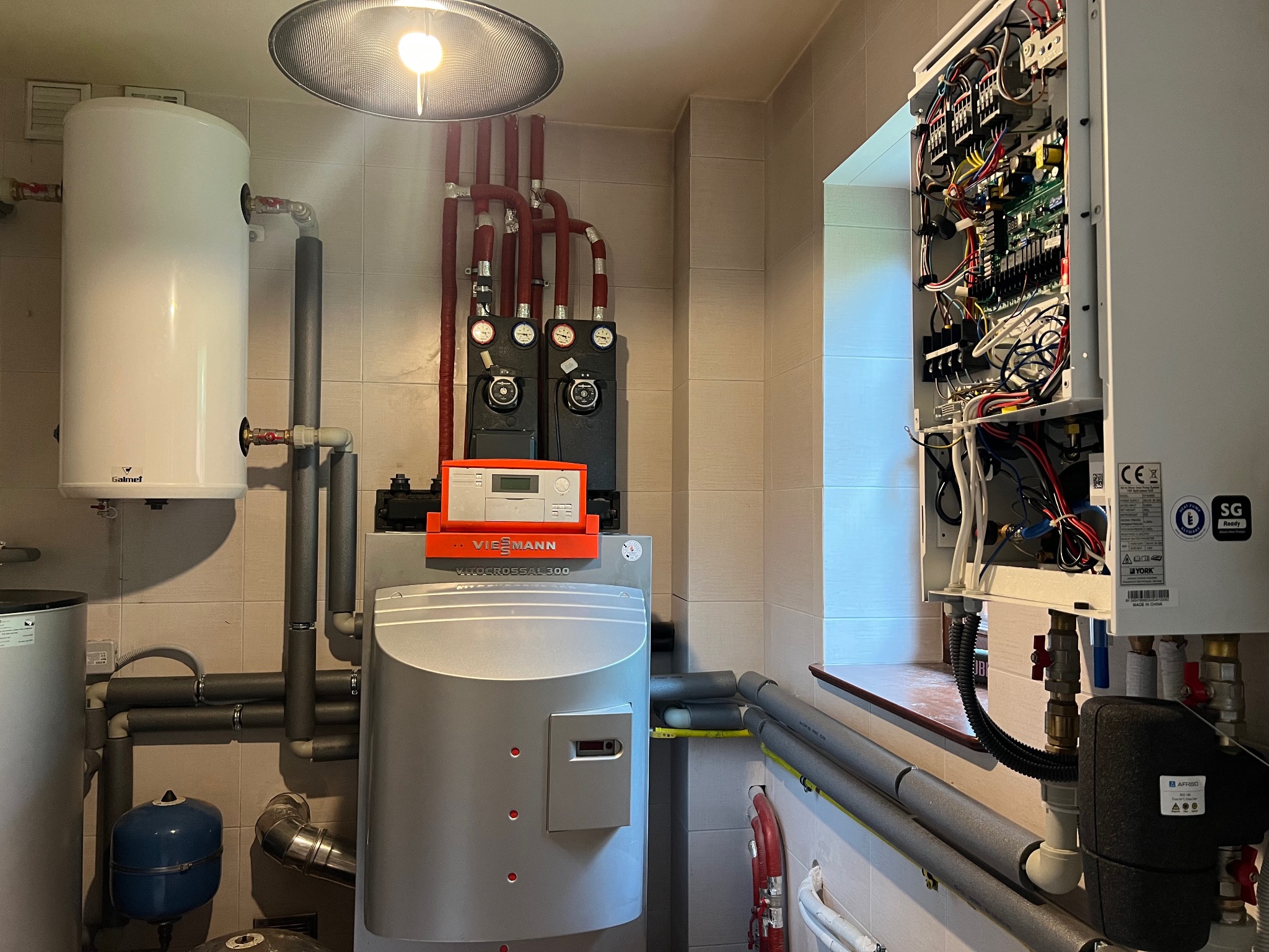Kotłownia z piecem Viessmann Vitocrossal 300 i zbiornikiem Galmet. Widoczne rury, zawory, manometry i instalacja elektryczna. Ujęcie w pomieszczeniu z jasnymi płytkami.