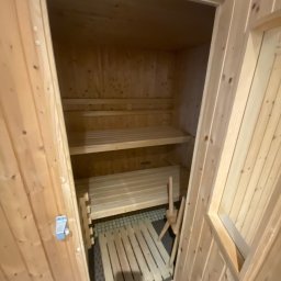 Komplexbud Yuliia Hedikova - Wnętrze nowej sauny z jasnego drewna, widoczne półki i siedziska, fragment pieca. Drzwi otwarte, z widocznym metalowym zamkiem.