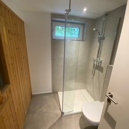 Komplexbud Yuliia Hedikova - Nowoczesna łazienka z kabiną prysznicową typu walk-in, wykończona szarymi płytkami i drewnianą boazerią, z widokiem na zieleń za oknem.