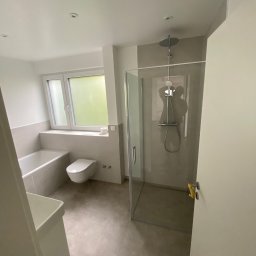 Komplexbud Yuliia Hedikova - Nowoczesna łazienka z kabiną prysznicową typu walk-in, umywalką, wanną i toaletą, wykończona w odcieniach szarości i bieli, z oknem zapewniającym naturalne światło.