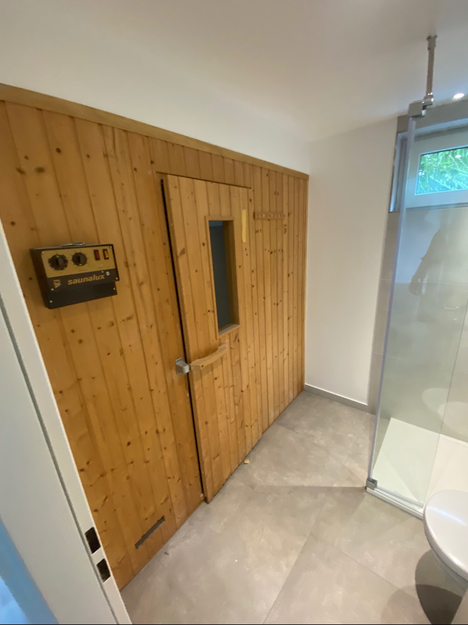 Wnętrze łazienki z drewnianą sauną z panelem sterowania Saunalux i kabiną prysznicową ze szklanymi drzwiami.