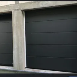 Dwie segmentowe, grafitowe bramy garażowe Hormann w surowym otoczeniu betonowych ścian i nadproży, widoczne detale montażowe.