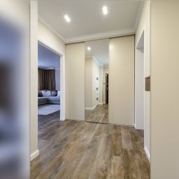 Wysmeble - Beżowa szafa przesuwna z lustrem w przedpokoju, widoczna drewniana podłoga i fragment salonu z sofą.