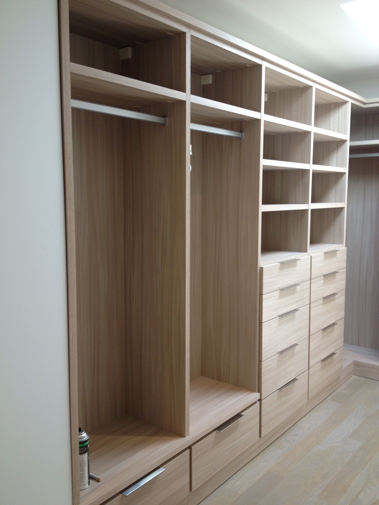 Jasna, drewnopodobna garderoba z szufladami i półkami, widoczna puszka z preparatem do pielęgnacji drewna, częściowo pusta.