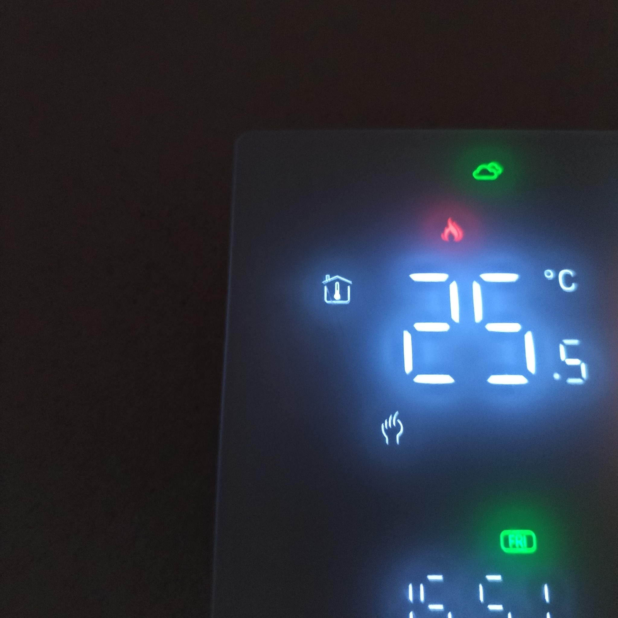 Wyświetlacz cyfrowy termostatu pokazujący temperaturę 25.5 stopni Celsjusza, ikonę płomienia, symbol domu z termometrem w środku, ikonę chmury i ustawiony dzień tygodnia na piątek.