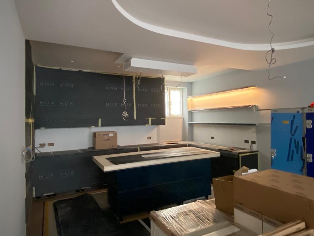 Wnętrze kuchni w trakcie montażu instalacji w Gdyni. Widoczne przygotowane ściany, wyspa kuchenna, oświetlenie podszafkowe i materiały budowlane.