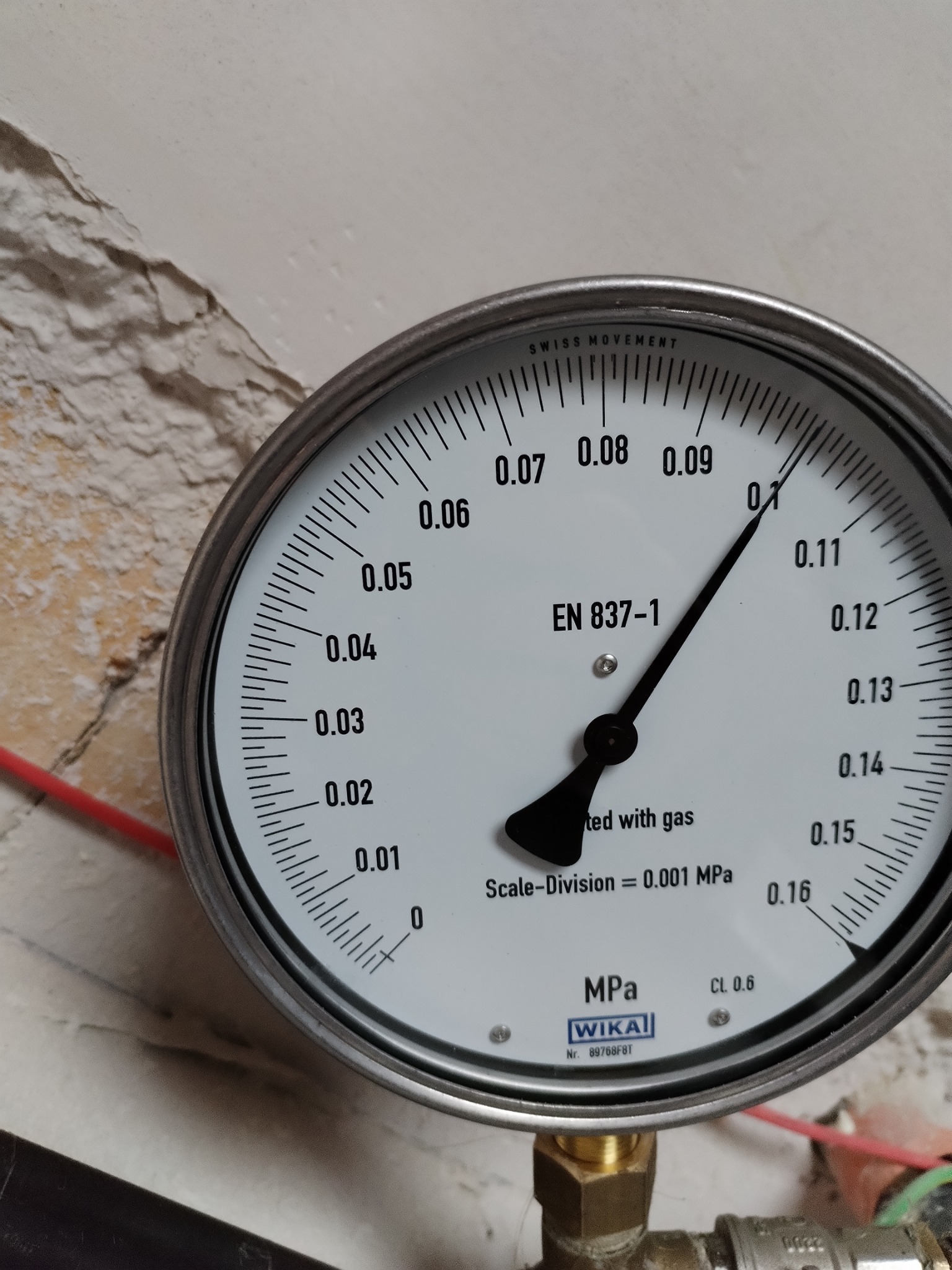 Manometr WIKA wskazujący ciśnienie gazu na instalacji, widoczny fragment instalacji oraz ściana z odpryskującą farbą.