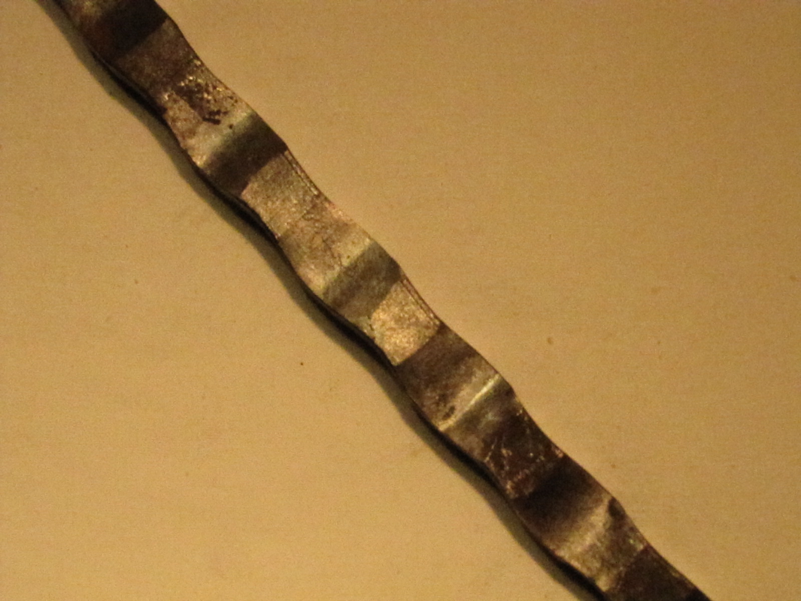 Detal walcowanej stali nierdzewnej z widocznymi śladami obróbki i refleksami światła na beżowym tle.