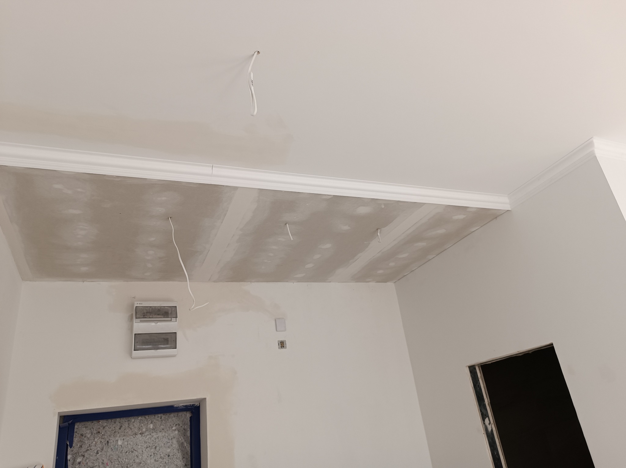 Sufit podwieszany z płyt kartonowo-gipsowych w trakcie montażu, widoczne łączenia płyt i wystające przewody elektryczne, listwa dekoracyjna na styku ściany i sufitu.