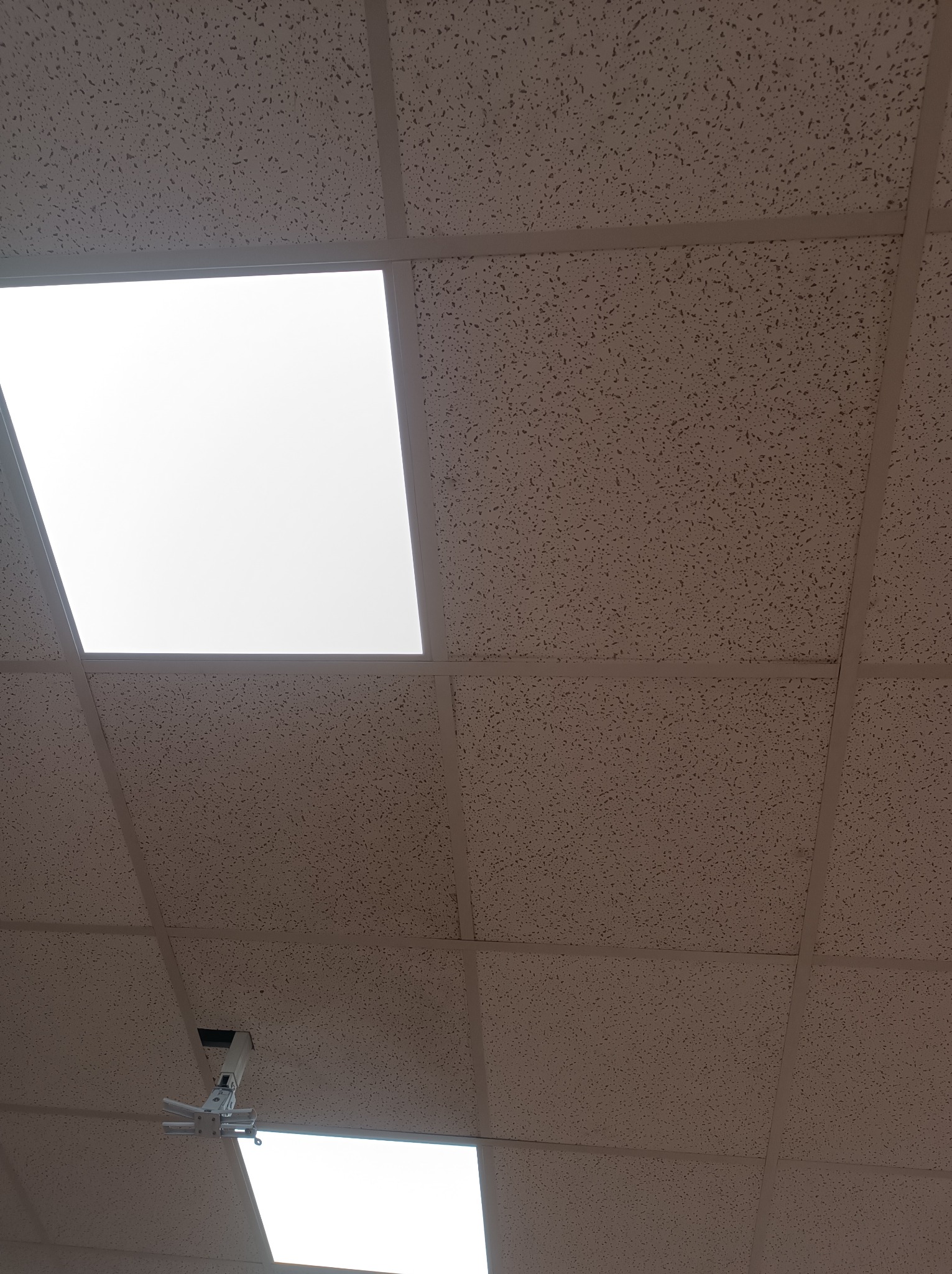 Kasetonowy sufit podwieszany z widocznym uchwytem do projektora i kwadratowymi panelami oświetleniowymi.