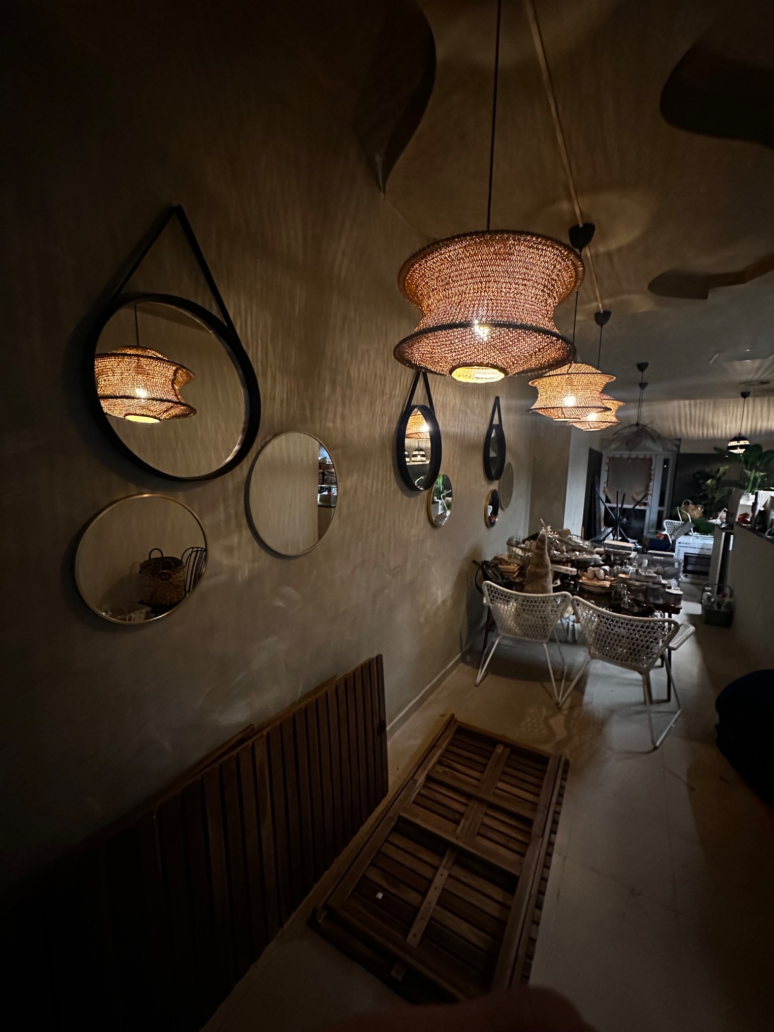 Wnętrze restauracji z dekoracyjnymi okrągłymi lustrami na ścianie, plecionymi lampami wiszącymi i drewnianymi panelami podłogowymi w trakcie montażu.