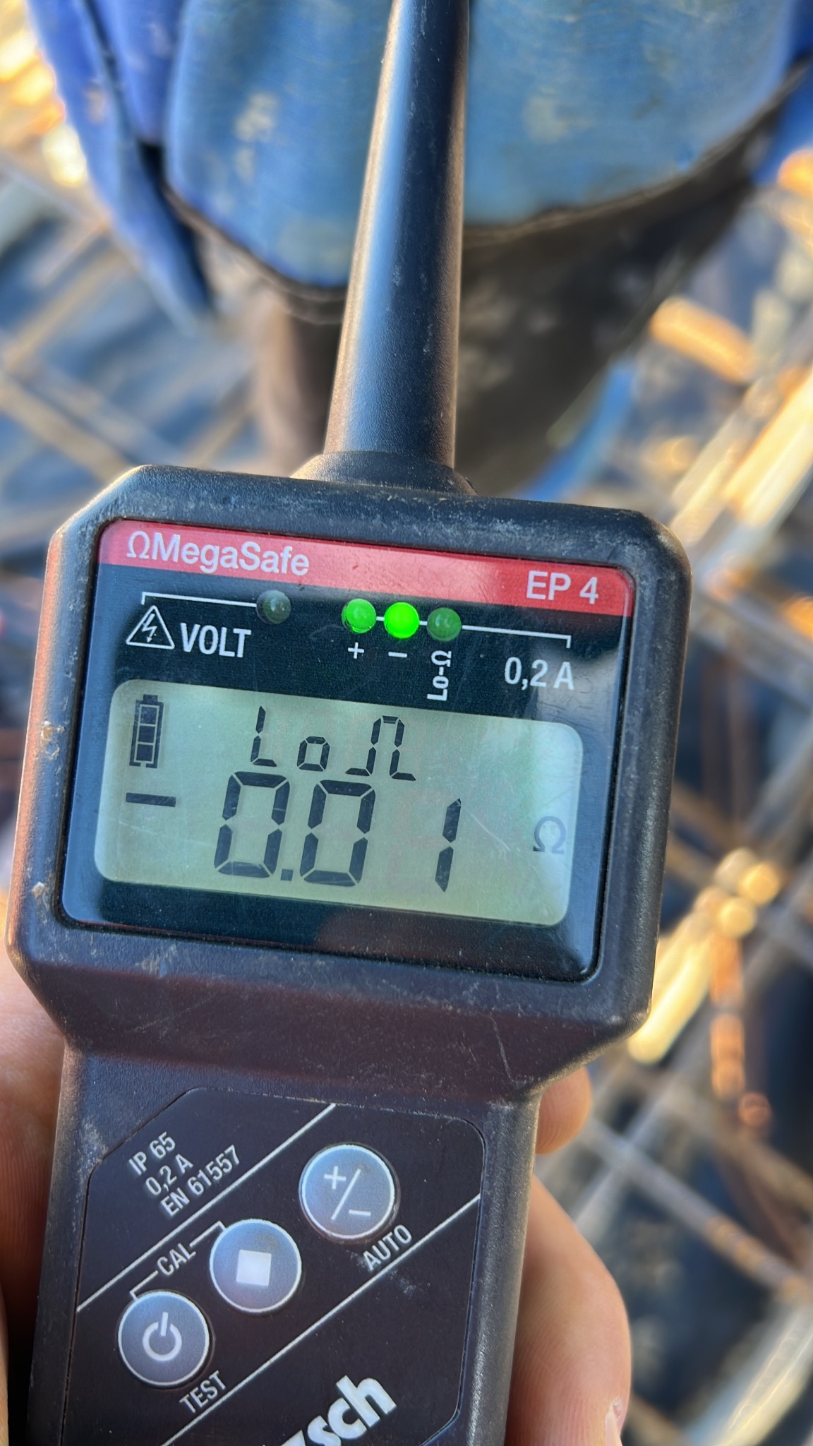 Miernik rezystancji uziomu OmegaSafe EP 4 z wyświetlaczem wskazującym 0.01 Ω, używany podczas prac zbrojarskich na budowie.