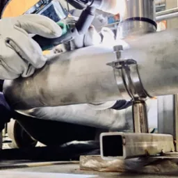 Spawanie rury ze stali nierdzewnej z użyciem spawarki TIG, widoczne iskry i osłona spawalnicza.