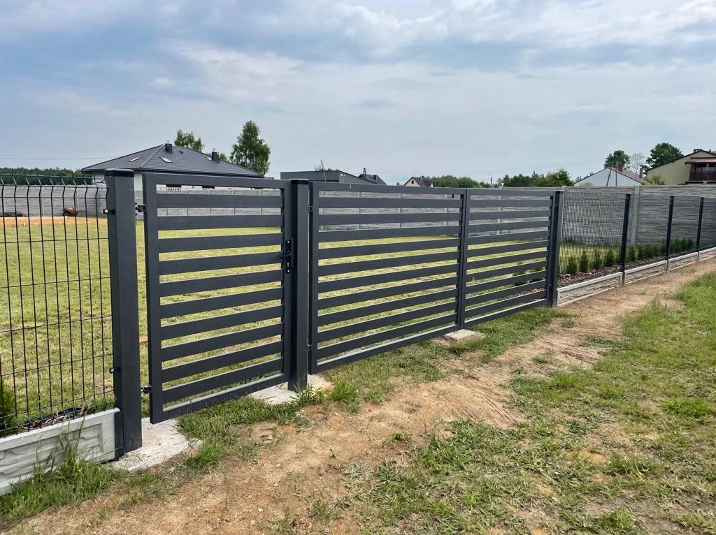 Nowoczesna, pozioma brama i przęsła ogrodzeniowe w kolorze grafitowym, z widocznym zamknięciem, na tle trawnika i domu jednorodzinnego.