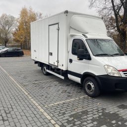 Perfekta - Biały furgon dostawczy zaparkowany na brukowanym parkingu w pochmurny dzień, widoczne jesienne liście na ziemi.