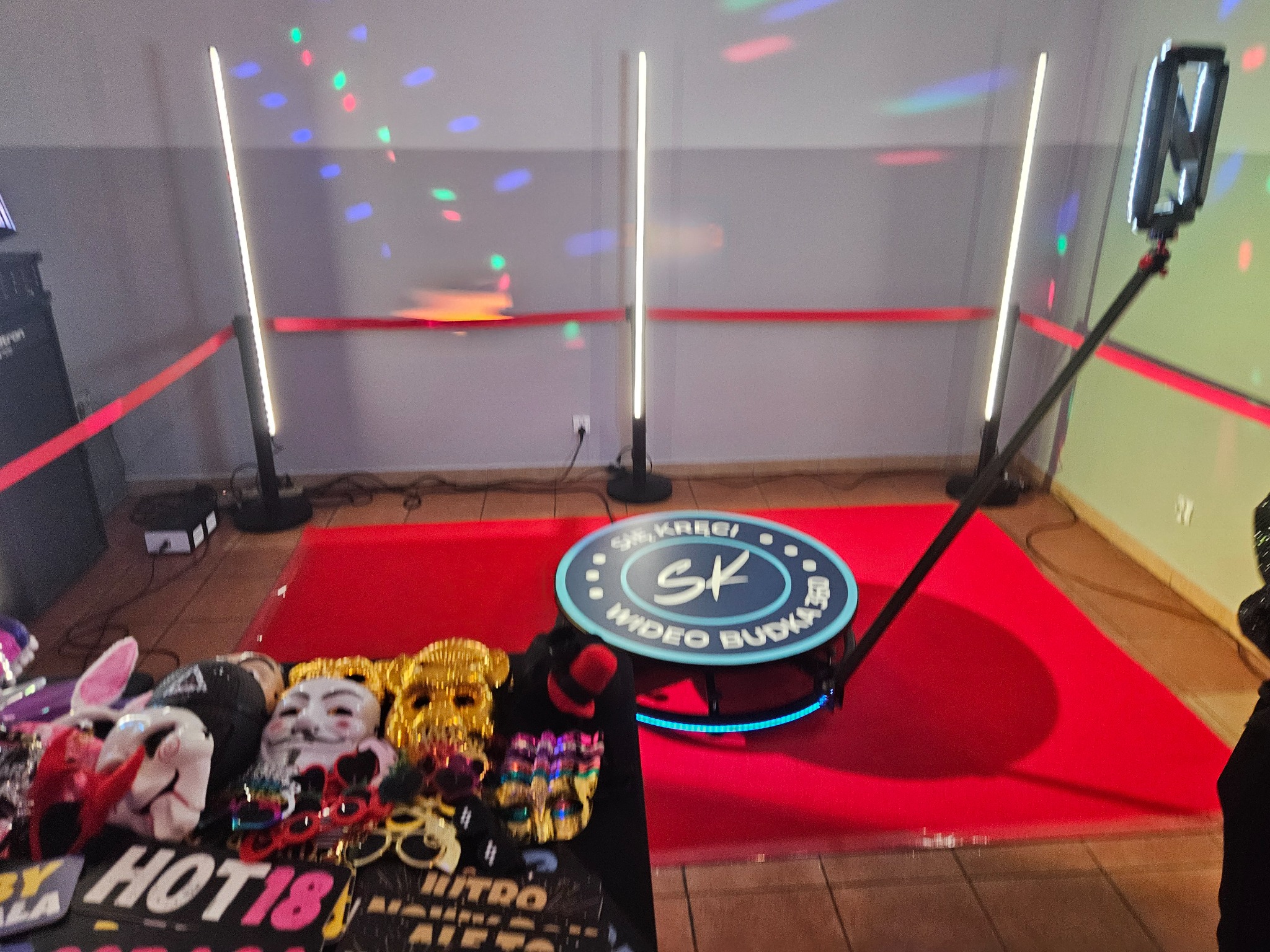 Kompletna, rozstawiona fotobudka 360 z rekwizytami: maski, okulary. Czerwony dywan, oświetlenie LED, efekty świetlne na ścianie. Gotowość do imprezy.