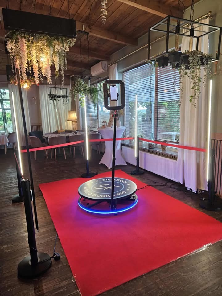 Kompletna fotobudka 360 na czerwonym dywanie w eleganckim wnętrzu z dekoracjami kwiatowymi. Gotowa do użycia na imprezie.